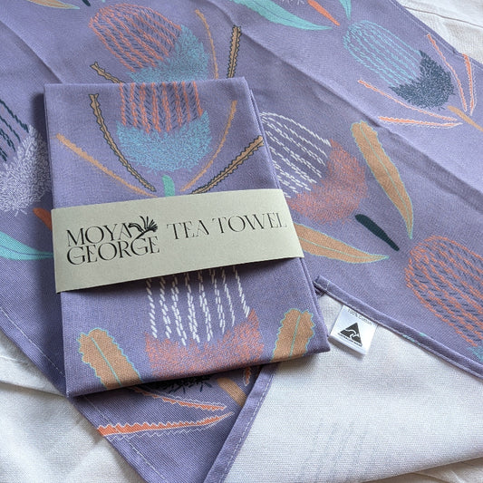 Purple tea towel with floral design and 'Moy George' branding on a white surface.