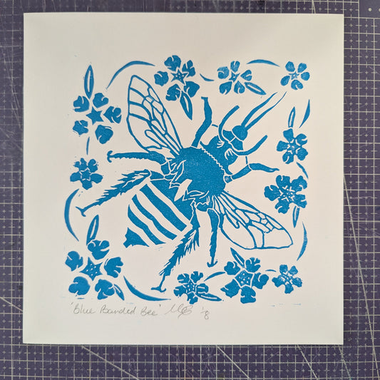 Blue bee and floral design on a white cardstock sheet, placed on a grid surface.